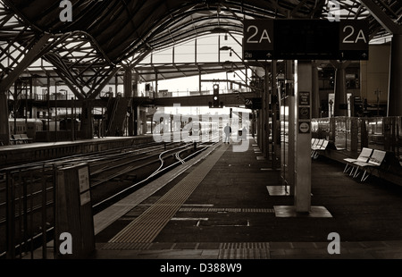 Ein einsamer Mensch ist gegen das Licht Silhouette, wie er auf einer leeren Plattform in einem Bahnhof auf einen Zug wartet. Stockfoto