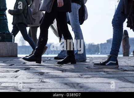 Eine Masse der Beine und Füße des venezianischen Touristen zu Fuß entlang der Uferpromenade am Markusplatz, Venedig, Italien. Stockfoto