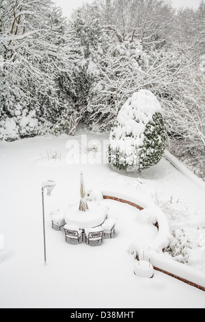 Schnee in einem Garten in Surrey, England, UK - mit Schnee bedeckten Terrasse Stühle und Tisch und Bäume und Äste mit Schnee bedeckt Stockfoto