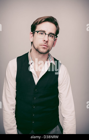 Mann in den zwanziger Jahren in schwarze Weste, weißes Hemd, graue Hosen und Brille sieht traurig. Stockfoto