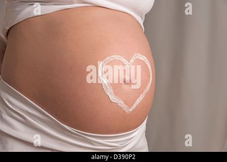 Junge Frau mit weißen Kleidern und ein Creme Herz auf ihrem Baby-Bauch Stockfoto