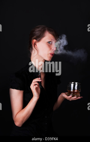 hübsche junge Frau mit einer elektrischen Zigarette, mit einem Glas Whiskey und schwarzem Hintergrund Stockfoto