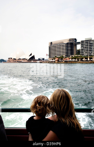 Mutter und Sohn schauen von der Rückseite einer Sydney-Fähre am Sydney Opera House und die Skyline von Sydney. Stockfoto
