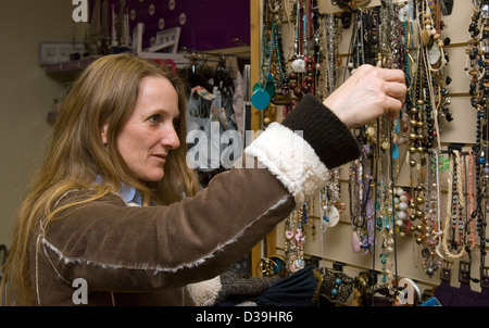 Frau Shopper durchlesen Schmuckstücke auf dem Display in Age UK Charity Shop, Godalming, Surrey, UK. Stockfoto