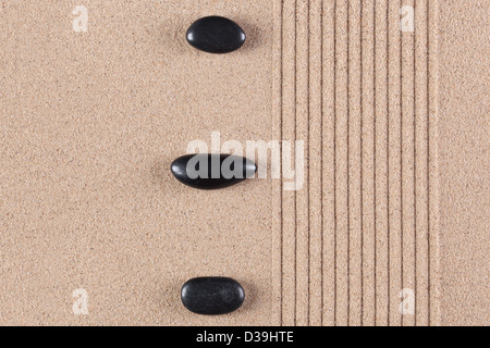 Drei schwarze Kieselsteine auf einen geharkt Sand Zen-Garten. Stockfoto