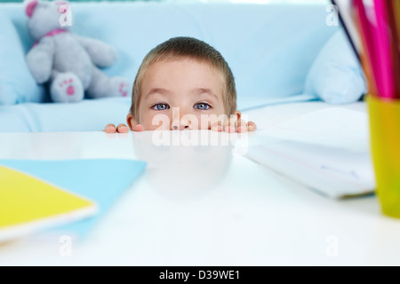 Verspielter kleiner Junge unter dem Tisch versteckt Stockfoto