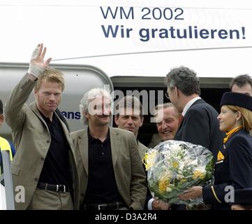 (Dpa) - Fußball-Team Torhüter und Kapitän Oliver Kahn (L) Wellen warten Fans neben (von L-r:) team Chef Rudi Voeller, Trainer Michael Skibbe und German Soccer Association Präsident Gerhard Mayer-Vorfelder als Team kommt am Flughafen Frankfurt/Main, 1. Juli 2002. Das Banner liest "WC-200 Stockfoto