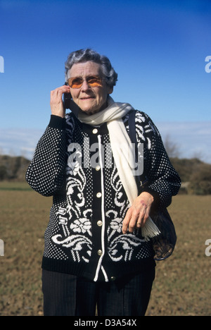 Ältere Frau mit ihrem Mobiltelefon auf dem Lande, die versuchen, ein Signal (entweder verloren oder Auto ist kaputt) Stockfoto