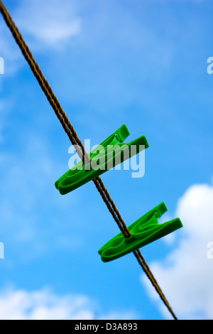 Zwei grüne Pflock auf einer Wäscheleine vor einem bewölkten blauen Himmel. Stockfoto