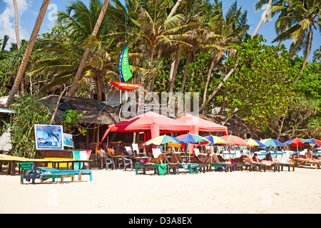 Die Touristen liegen unter Sonnenschirmen am Strand von Mirissa, südlichen Sri Lanka außerhalb der Wadiya Magical Strandbar. Stockfoto