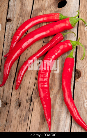 Fünf lebendig und frisch geerntete rote Chilischoten auf einem alten Holztisch. Stockfoto