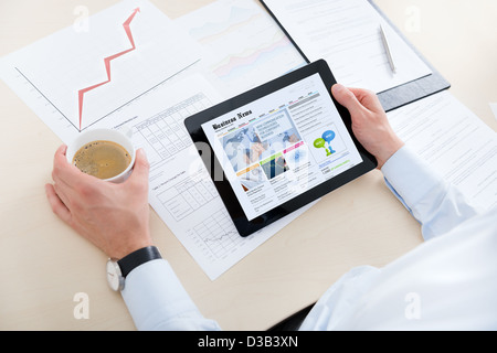 Geschäftsmann am Arbeitsplatz Kaffee zu trinken und auf der Suche nach neuesten Wirtschaftsnachrichten auf modernen Digitalrechner. Stockfoto