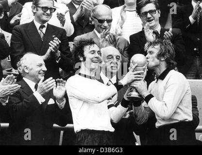 (Dpa-Dateien) - Franz Beckenbauer (2. v. L), dann deutsche Mannschaftskapitän und Torhüter Sepp Maier (R) ihre Trophäe, schätzen während deutsche Präsident Walter Scheel (L) begrüßt, nachdem Deutschland die Fußball-Weltmeisterschaft in München, 7. Juli 1974 gewann. Deutschland besiegt die Niederlande im Finale mit 2:1. Stockfoto