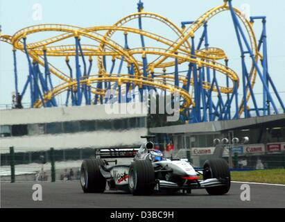 (Dpa) - Rennen finnische Formel 1 pilot Kimi Raeikkoenen vorbei an eine Achterbahn von einem benachbarten Kirmes, beim Training in Suzuka, Japan, 11. Oktober 2002. Stockfoto