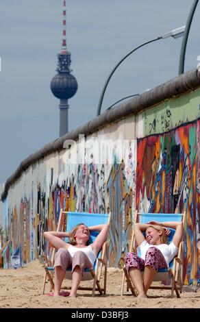 (Dpa) - zwei junge Frauen amüsieren wie sie ein Sonnenbad in der East Side Gallery in Berlin, 27. Juni 2003 nehmen. Im Hintergrund der Berliner Fernsehturm. Die East Side Gallery, einem Teil der ehemaligen Berliner Mauer, bietet Bilder von internationalen Künstlern und entstand als Denkmal kurz nach th Stockfoto