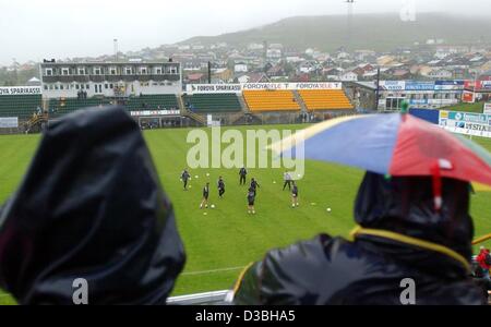 (Dpa) - zwei Menschen Regen mit Hauben und einen Regenschirm halten aus wie sie die deutsche Fußball-Team-Training in Tórshavn, Färöer Inseln, 10. Juni 2003 beobachtest. Die Teams aus Deutschland und den Färöer Inseln spielen ein Qualifikationsspiel für die Europameisterschaft im Jahr 2004. Während Tempe Stockfoto