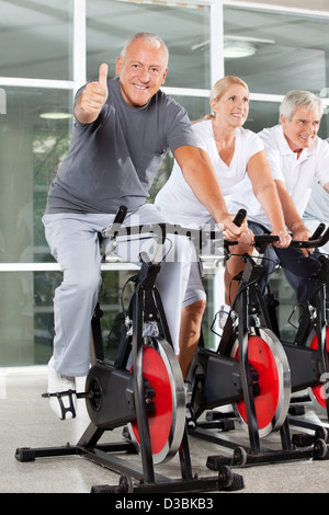 Happy senior woman auf spinning Bike Daumen hochhalten, im Fitness-Studio Stockfoto