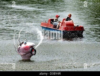 (Dpa) - das spucken Kunstwerk "Der Wasserspucker" (Wasser-Spitter) spritzt Wasser während zwei Jungs Ansatz in ihre Pedal Boot im Olympiasee München, 1. August 2003. Die Wasser-Spitter ist ein Kunstwerk von Thadeus Hueppi. Stockfoto