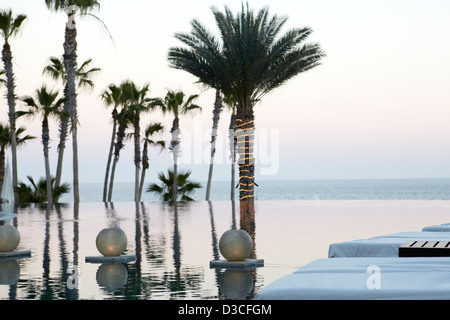 Resort-Infinity-Pool bei Sonnenuntergang Dämmerung mit schwimmenden Laternen und Lichter auf der Palme. Stockfoto