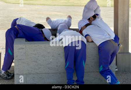 Gruppe von neugierig, junge japanische Schuljungen im Sport Uniformen Biegung über Rand eines Brunnens, wie sie die Welt um sie herum erkunden. Stockfoto