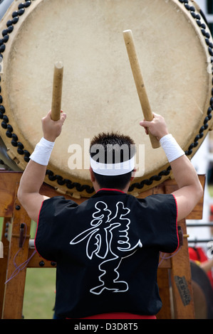 Ein Mann trägt einen Festival Happi Mantel schlägt einen musikalischen Rhythmus auf eine Odaiko, die Japaner mit Holzschlegel Trommel. Stockfoto