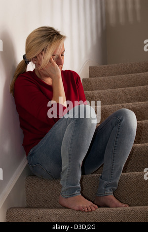 Blonde Frau sitzt allein auf der Treppe, zu Hause, auf der Seite ihr Gesicht verärgert die hand. Stockfoto