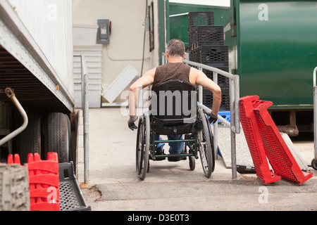 Laden Hafenarbeiter mit Querschnittslähmung im Rollstuhl Rampe hinauf, neben einem LKW Stockfoto