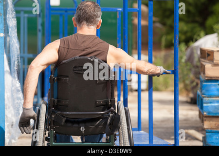 Laden Hafenarbeiter mit Querschnittslähmung im Rollstuhl bewegen einen Hand-LKW Stockfoto