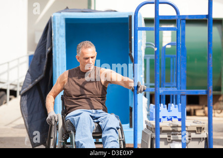 Laden Hafenarbeiter mit Querschnittslähmung im Rollstuhl bewegen einen Hand-LKW Stockfoto