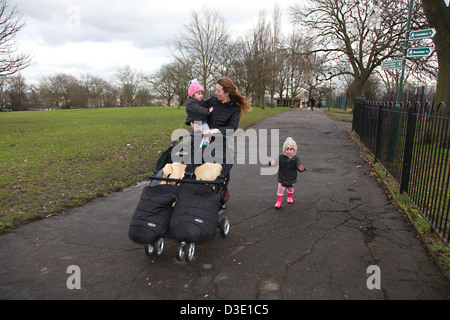 Junge Mutter im Park schieben einen Twin Buggy mit ihren zwei Kleinkinder. Stockfoto