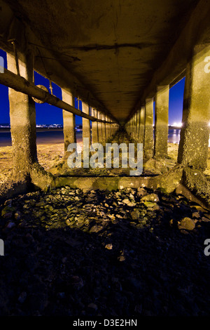 Unendlicher Blick unter einer alten Brücke in der Nacht am Strand. Stockfoto