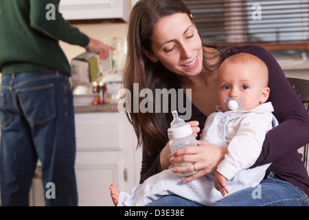 Baby in Mutters Arm mit Schnuller und Vater Saft in Strömen Stockfoto