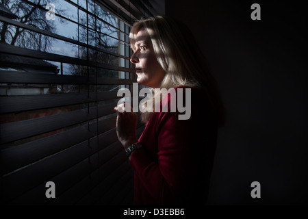 Profil einer Frau im Schatten Blick durch ein Fenster Licht strömt durch die Blinds auf ihr Gesicht. Modelleigenschaft veröffentlicht. Stockfoto