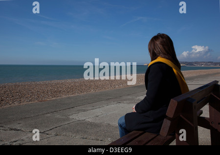 Zurück zur Kameraaufnahme ein Frau Mantel und Schal sitzen allein Blick auf das Meer, bedeutet der Verlust eines lieben Menschen. Stockfoto