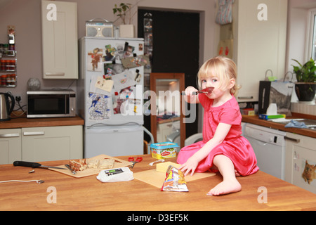 Kleinkind sitzt alleine auf einem Küchentisch Butter Essen Stockfoto