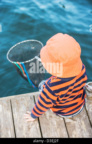 Kleines Kind sitzt auf Dock am Meer beobachten das Wasser mit Fischernetz in der hand Stockfoto