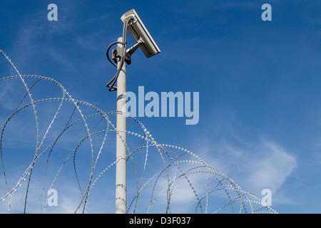 Überwachungskamera und Stacheldraht gegen blauen Himmel Stockfoto