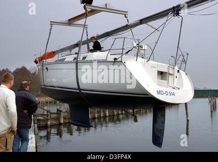 (Dpa) - eine Gruppe von Männern, einer von ihnen sitzt auf dem Boot, zu sehen wie die Segelyacht mit einem Kran auf die Wasseroberfläche an die Segel, auf der viele Sport und Yacht-Häfen rund um den See-Müritz in der Nähe Waren, Deutschland, 28. März 2003 angehobenen. Vor ein paar Tagen ist das Eis auf dem See geschmolzen entfernt so dass des Raums offen für Segel- und Wassersport-Aktivitäten. Stockfoto