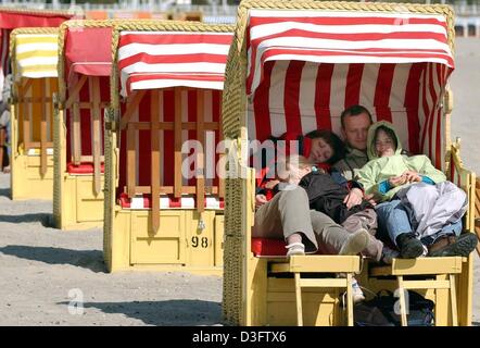 (Dpa) - eine Familie sitzt dicht beieinander um einander im Strandkorb in Travemünde, Deutschland, 18. April 2003 zu wärmen. Wegen der kalten Temperaturen ist der Strand menschenleer. Die liegen am Strand, auf dem Sand stehen überwiegend leer. Die traditionellen deutschen Strandkorb bietet Schutz gegen Sonne, Wind oder Regen und finden Sie an der deutschen Küste der Nordsee und der Ostsee. Stockfoto