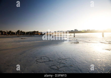 junges Paar am Strand bei Sonnenuntergang; Loveheart und Initialen geschnitzt in den sand Stockfoto