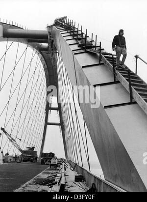 Bauherren haben die letzten Arbeiten an den Bögen der Brücke im April 1963. Sonnenuntergang hinter der Brücke (undatiertes Bild). Die Brücke über den Fehmarnsund in der Ostsee verbindet das Festland mit der Insel Fehmarn. Die kombinierte Straßen- und Eisenbahn-Brücke wurde der Öffentlichkeit am 30. April 1963 eröffnet. Stockfoto