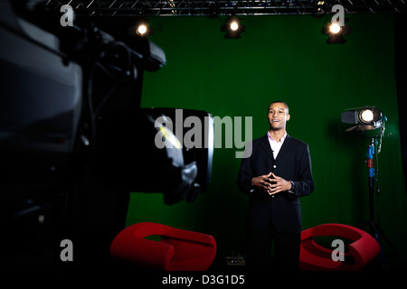 TV-Moderatorin in einem Greenscreen-Studio mit Fernsehkamera außerhalb des Fokus im Vordergrund. Stockfoto