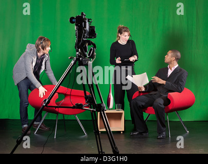 Ein Crew-Mitglied ordnet Möbel während der Aufnahmeleiter Gespräche an den Vortragenden über ein TV-Studio setzen. Stockfoto