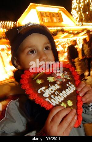 (Dpa) - drei-jährigen Damian nimmt einen Bissen von einem Lebkuchenherz trägt die Schrift "Frohe Weihnachten" auf dem Weihnachtsmarkt in Frankfurt am Main, 9. Dezember 2003. Stockfoto