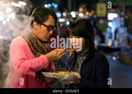 Ein paar junge Touristen Essen aus einer Garküche auf dem Nachtmarkt in Pai, Mae Hong Son Provinz, Thailand Stockfoto