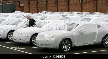 (Dpa) - steht ein Arbeiter der britischen Automobilhersteller Bentley Motors auf der Betriebsfläche zwischen Neuwagen, die von einer weißen Plane von Wetterfaktoren in Crewe, England, 26. Oktober 2004 geschützt sind Stockfoto