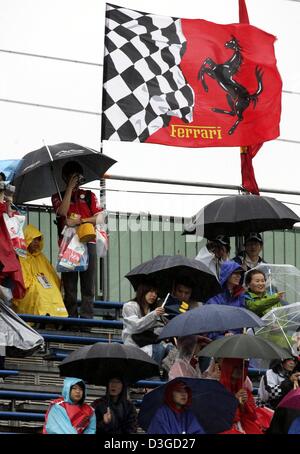 (Dpa) - Formel-1-Fans unter Sonnenschirmen vor einer Ferrari-Flagge weht in den starken Wind in Suzuka International Racing Course in Suzuka, Japan, 8. Oktober 2004 sitzen. Wegen einen herannahenden Taifun könnte Rennen am Samstag und eventuell sogar am Sonntag abgesagt werden. Der Grand Prix von Japan wird voraussichtlich am Sonntag, 10. Oktober 2004 stattfinden. Stockfoto