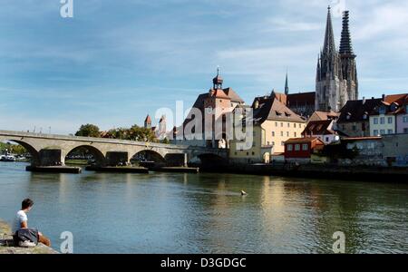 (Dpa) - eine Frau sitzt am Ufer der Donau in der Nähe der steinernen Brücke (Hintergrund) und blickt auf die Altstadt mit der Kathedrale von St. Peter in Regensburg, Deutschland, 1. September 2004. Die Stadt Regensburg hat in diesem Sommer als UNESCO-Weltkulturerbe aufgeführt werden angewendet. Stockfoto