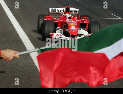 (Dpa) - flag brasilianischen Formel 1 pilot Rubens Barrichello (Ferrari) Rennen vorbei an jubelnden Ferrari-Team, die Welle den Italiener, wie er großen Preis von China auf dem neuen Shanghai International Circuit in Shanghai, China, 26. September 2004 gewinnt. Stockfoto