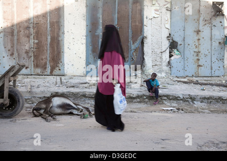 Eine Hijab gekleidete Frau geht vorbei an einen toten Esel in der Innenstadt von Mogadischu, Somalia. Stockfoto